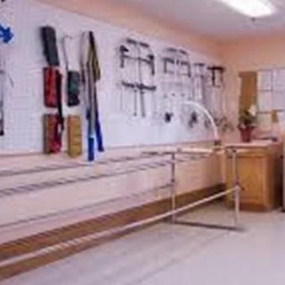 A physical therapy room equipped with parallel bars and various rehabilitation tools hanging on the wall.