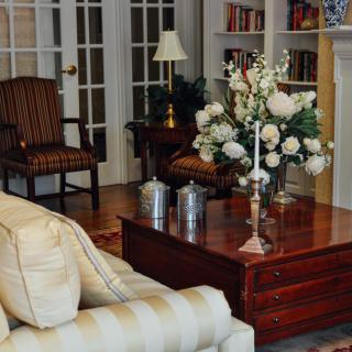 A cozy living room with elegant furnishings, featuring a sofa, coffee table with floral arrangement, and a bookshelf in the background.