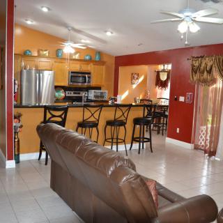 A modern open-concept kitchen and living area with bright colors, featuring a set of bar stools and stainless steel appliances.