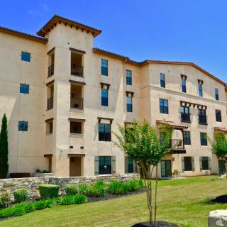 A modern apartment building with well-maintained landscaping under a clear blue sky.