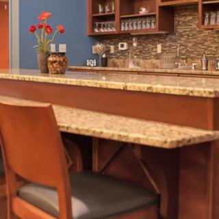 A modern bar setup with a granite countertop, wooden chairs, and decorative elements.