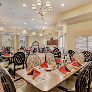 An elegantly set dining room with neatly arranged tables and chairs, featuring red napkins and ambient lighting.