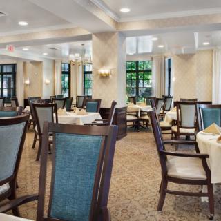 An elegant dining room with neatly arranged tables and chairs, softly lit by classic light fixtures.