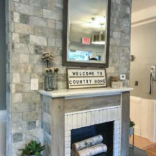 A rustic-style fireplace with a mirror above and a welcoming 'Country Home' sign.