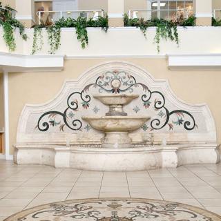 A decorative indoor fountain with ornate detailing, surrounded by potted plants and situated on a tiled floor.