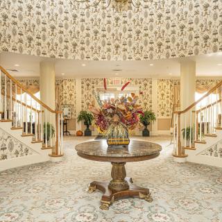 A luxurious lobby with a central floral arrangement, surrounded by decorative wallpaper and elegant staircases.