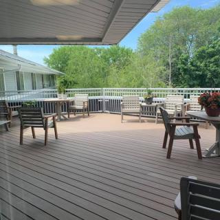 A spacious outdoor deck with tables and chairs, sheltered by an awning, surrounded by lush greenery.