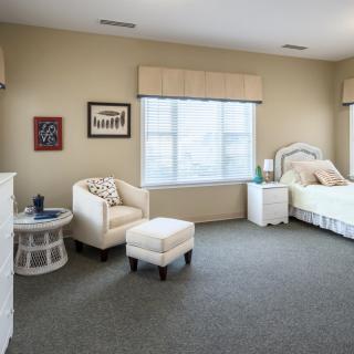 A cozy bedroom featuring a comfortable bed, an armchair with an ottoman, and a large window letting in natural light.