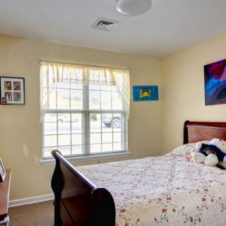 A cozy bedroom with a large window allowing natural light to fill the space, featuring a neatly made bed and decorative artwork on the walls.