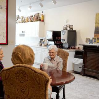 Elderly individuals sitting around a table in a kitchen, engaged in conversation.