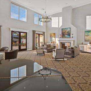 A spacious and modern living room with high ceilings, large windows, elegant chandeliers, and comfortable seating around a central fireplace.