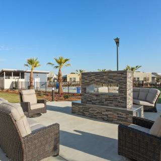 A sunny outdoor patio area with a modern fireplace and comfortable seating surrounded by palm trees.
