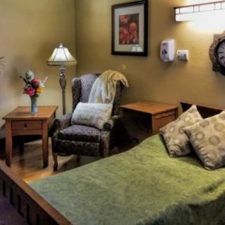 A cozy bedroom with warm lighting, featuring a bed, an armchair, and a bedside table with decorative items.