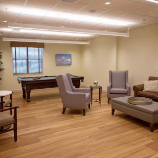 A modern lounge area featuring comfortable seating arrangements and a pool table, with wood flooring and neutral decor.