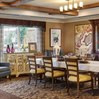 A warmly decorated dining room with a large table and chairs, featuring elegant artwork and a window view.