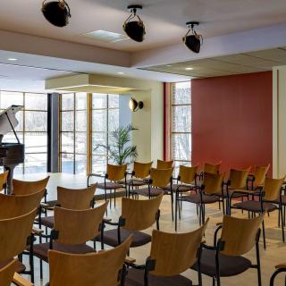 An empty conference room with arranged chairs and a piano near the windows.