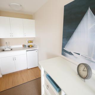 A minimalist kitchen with white cabinets and a sailboat painting on the wall.