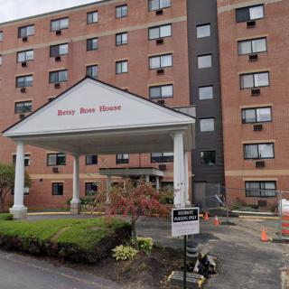 The image shows the entrance of a multi-story apartment building with a covered entryway and some landscaping.