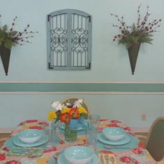 A dining table set with turquoise dinnerware and a floral centerpiece, accompanied by decorative wall accents.