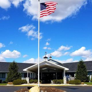 A building entrance with an American flag flying against a blue sky and clouds.