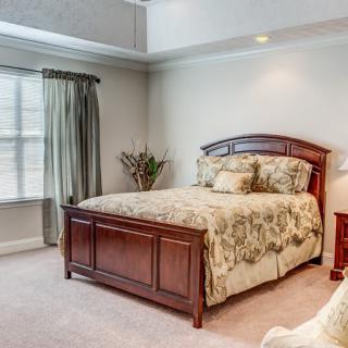 A cozy bedroom featuring a wooden bed frame, floral bedding, and natural light from a large window with curtains.