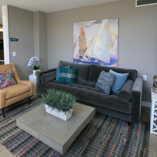 A modern living room featuring a grey sofa, an armchair, a coffee table with a plant centerpiece, and abstract artwork on the wall.
