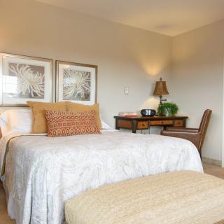 A cozy bedroom with a neatly made bed, decorative pillows, and a desk with a lamp.