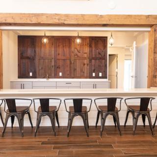 A modern kitchen with a large counter and bar stools, featuring pendant lighting and a wooden floor.