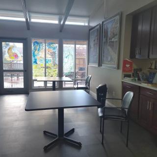 A bright cafeteria space with tables and chairs, decorated with colorful artwork on the windows.