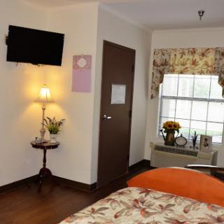 A cozy and well-decorated room featuring a TV, a bedside lamp, and floral curtains by the window.
