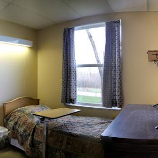 A cozy hospital room featuring a bed, table, and window with natural light.