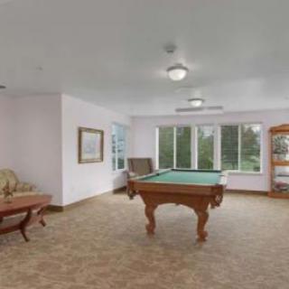 A spacious billiards room featuring a pool table and comfortable seating, with large windows providing natural light.