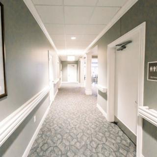 A long hallway with a patterned carpet, lined with doors and softly lit by ceiling lights.