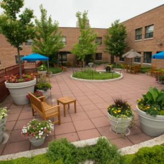 A serene courtyard with benches, plants, and patio umbrellas surrounded by a brick building.