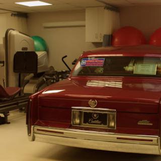A red car parked in a garage alongside exercise equipment and fitness balls.