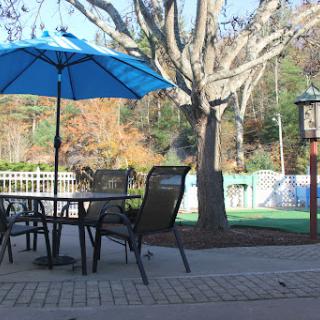 A serene outdoor patio setup with a blue umbrella, surrounded by trees and scenic views.