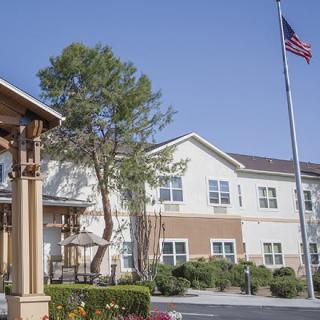 A two-story building with a flagpole and tree in front, set against a clear blue sky.