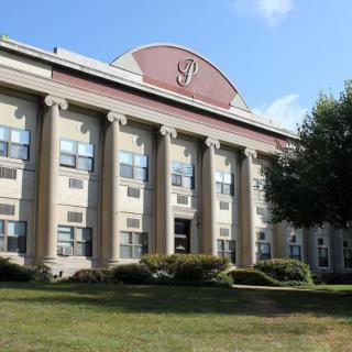 A classical building with columns and a well-maintained lawn in front.