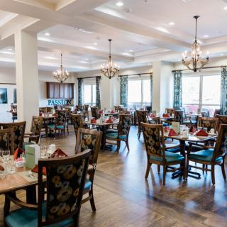 A spacious and elegantly decorated dining area with several tables and chairs, featuring chandeliers and natural lighting.