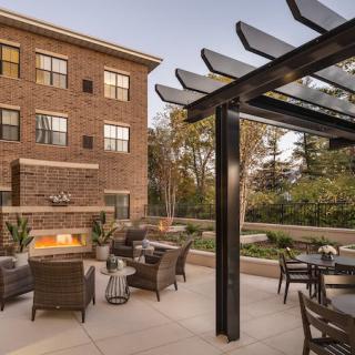A cozy apartment patio featuring comfortable outdoor seating, a modern fireplace, and a stylish pergola.