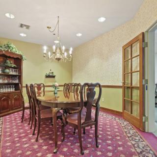 A formal dining room with an elegant wooden table and chairs, a chandelier overhead, and a patterned carpet underfoot.