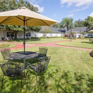 A sunny outdoor patio with tables and chairs under large umbrellas set in a grassy garden area.