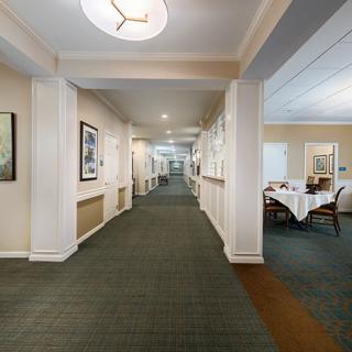A well-lit hallway with artwork on the walls and a dining area to the side.