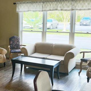 A cozy living room with a sofa and chairs around a coffee table, illuminated by natural light from the windows.
