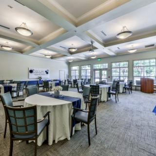 A spacious and well-lit event hall with round tables set for a gathering.