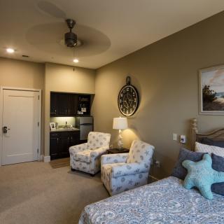 A cozy bedroom with a seating area, featuring two patterned chairs, a bed adorned with pillows, and stylish decor in neutral tones.