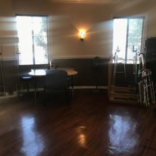 An empty room with wooden floors, a few tables and chairs, and two windows letting in natural light.