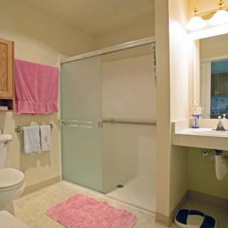 A modern bathroom with a sliding glass shower door, pink bath mat, and towels.