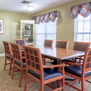 A well-lit conference room with a long meeting table surrounded by wooden chairs and two large windows.