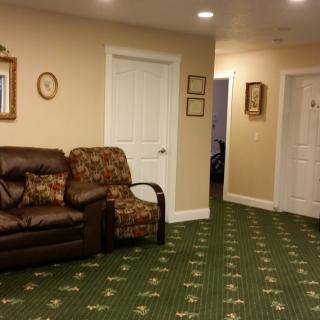 A cozy living room with a patterned carpet, leather sofa, and armchair, adorned with wall decorations.